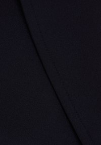Gros plan d’un tissu bleu marine foncé avec une couture visible le long d’une jointure sur un matériau lisse et tissé serré.