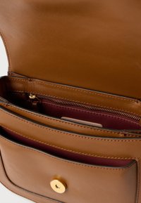 Interno di borsa in pelle marrone con fodera color vinaccia e tasca con cerniera. Chiusura in metallo dorato visibile nella tasca anteriore. Design semplice e rettangolare.