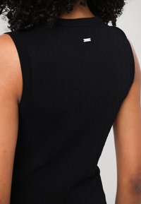 Crna bezrukavna majica s teksturiranim uzorkom dijamanta, rebrastim izrezom i otvorima za ruke, s malom srebrnom oznakom na stražnjoj strani.