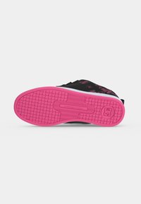 Baskets noires avec semelle rose vif montrant le motif de la semelle et le logo de la marque sur un fond clair et lisse.