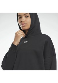Schwarzer Kapuzenpullover mit langen Ärmeln, oversized Schnitt und einem kleinen weißen Logo auf der Brust. Glatte Textur und minimalistisches Design.