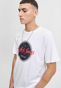 Witte katoenen t-shirt met een ronde zwarte grafiek en rode tekst "Jack & Jones" met een gestreepte rand. Korte mouwen en ronde halslijn.