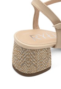 Beżowe sandały na platformie z plecionym teksturowanym obcasem. Design pasków zawiera gładką skórę i lekko wyściełaną wkładkę z detalem logo.