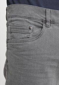 I jeans in denim grigio presentano una texture liscia, un design tradizionale a cinque tasche e un'applicazione di bottone metallico in vita.