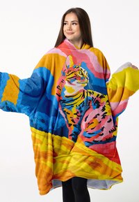 Kolorowy, ponadwymiarowy koc-hoodie wykonany z miękkiego, pluszowego materiału. Zawiera dużą grafikę kota na tle o żywych kolorach przypominających zachód słońca.