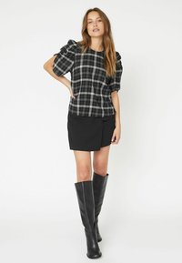 Tricou în carouri alb-negru cu mâneci scurte puff, asortat cu o fustă neagră încrețită și cizme de piele negre până la genunchi.