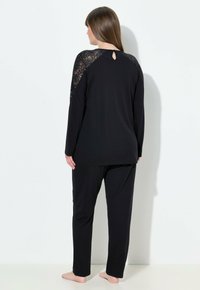 Conjunto de ropa de estar negro que incluye una camiseta de manga larga con detalles de encaje en los hombros y un escote en forma de ojo de cerradura, acompañado de pantalones a juego. Tejido suave.