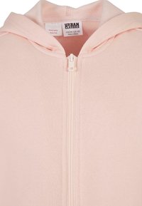 Ljusrosa zip-up hoodie med en mjuk tygtextur, en framfäste dragkedja och en huva med dragsko. Etikett synlig inuti kragen.