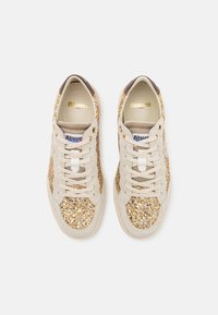Zapatillas de piel beige con detalles de brillo dorado, con puntera redonda, cordones planos y una etiqueta de logo en la lengua. Textura suave.