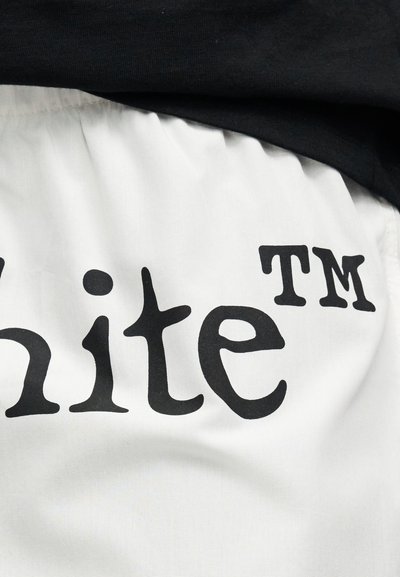 Biele tkanivo s čiernym štýlovo upraveným textom, ktorý čiastočne zobrazuje "ite TM" a čierny odev navrství nad ním.