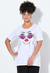 T-shirt blanc à manches courtes ornée d'un dessin au trait noir d'un visage avec des lunettes de soleil violettes et des lèvres rouges. Tissu doux, coupe ample.