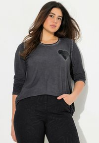 Zwarte longsleeve shirt met een ronde hals en een sequins hartdetail op de borst, gecombineerd met zwarte textuurbroek.