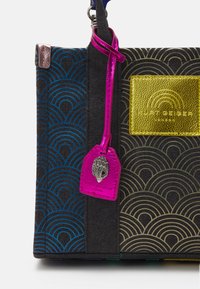 Torebka wielokolorowa z geometrycznym wzorem fal, z błyszczący różowym breloczkiem, złotą naszywką z logo i kontrastującymi fakturami.