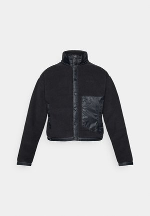 Chaqueta negra con un cuerpo de forro polar, acentos de nailon brillante, cuello alto, cierre a presión y un bolsillo en el pecho izquierdo con una textura contrastante.