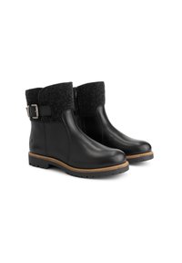 Een paar zwarte enkelboots met een getextureerde wolaccul cuff, zijritsen, gespsluitingen en een bruin gestikt zool op een witte achtergrond.