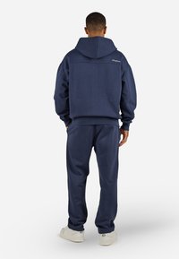 Navy blue hoodie with a hood, ribbed cuffs, and a relaxed fit, paired with matching joggers and white sneakers. The fabric appears soft and textured.