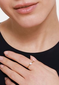 Anello d'oro con una perla rotonda liscia come accento posato su un dito di donna, mostrando un primo piano del tono della pelle e un design minimalista.