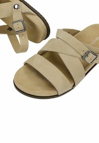 Sandales en daim beige avec trois larges brides sur le pied et une bride à boucle réglable autour de la cheville.