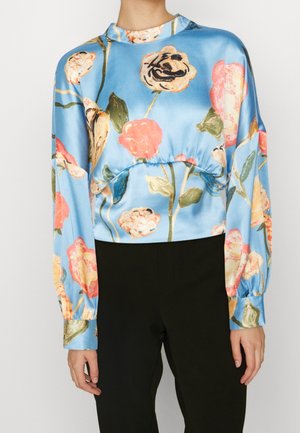 Bloemendruppelmuster blouse in blauwe satijn met lange pofmouwen, een hoge halslijn en een gathered taille; gecombineerd met zwarte broek.