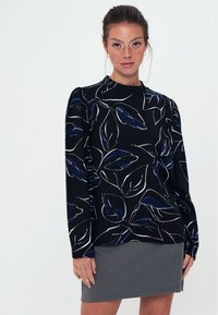 Blusa nera con motivo floreale bianco e dettagli blu navy; presenta maniche lunghe e collo rotondo. Abbinata a una gonna grigia.
