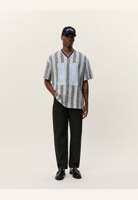 Camisa de manga curta riscada em cinza e branco com o número "11" em azul, combinada com calças escuras e um boné preto com texto branco.