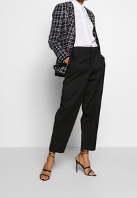 Rutigt blazer i marinblått och vitt, vit skjorta, högmidjade svarta byxor och svarta klackar med remmar, som visar en strukturerad silhuett.