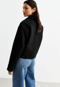 Svart kort sweatshirt med långa ärmar och klassisk krage, i kombination med ljusblå högmidjade jeans. Slät textur, minimalistisk design.