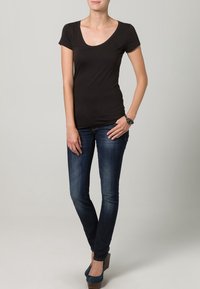 Svart kortärmad T-shirt med djup u-ringning, i kombination med mörkblå smala jeans och teal klackskor. Enkelt, figurnära design.