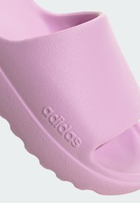 Ružičaste Adidas japanke s teksturiranom površinom, širokim remenom i konturiranim oblikom s debelim potplatom. Logotip je utisnut sa strane.