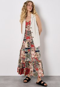 Weißes Nadelstreifen-Weste über einem maxi Kleid mit verschiedenen Mustern, floralem und Patchwork-Design, kombiniert mit schwarzen Riemchensandalen.