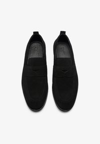 Sorte semskede slip-on sko med flat såle, med en dekorativ rem og subtile stikninger overover.