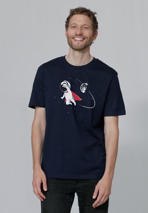 Marineblauwe katoenen t-shirt met een cartoonfiguur in een ruimtepak met een rode cape, ruimte-elementen en verspreide sterren op de achtergrond.