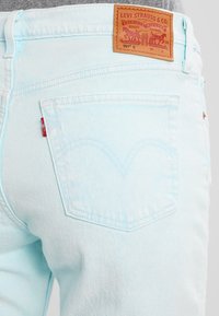 Jeans de mezclilla azul claro con una etiqueta de cuero en la parte posterior que muestra el logo de Levi Strauss, dos bolsillos traseros y detalles de costura blanca.