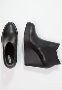 Botines negros de cuña con parte superior de cuero liso y paneles laterales elásticos, con suela gruesa de goma texturizada.