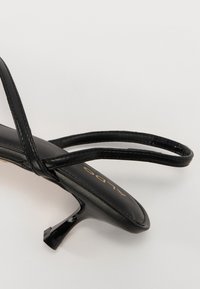 Sandal in pelle nera con tacco a spillo e fasce incrociate. Realizzato in pelle liscia, con punta arrotondata e piatta e un sottile marchio dorato.