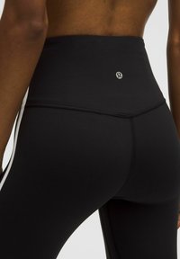 Črne legice z visokim pasom, narejene iz raztegljivega materiala, s slim fit krojem in logotipom na zadnji strani, ter kontrastnimi stranskimi črtami.