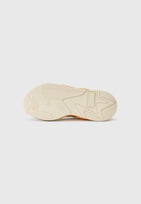 Suola della scarpa con una texture ondulata in colore crema, realizzata in materiale gommoso, con un accento arancione. Il motivo di battistrada include esagoni e creste.
