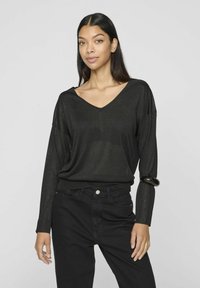 Musta, pitkähihainen neulepaito, jossa on V-kaula-aukko, rento malli ja hieman läpinäkyvä rakenne, yhdistettynä mustiin korkeavyötäröisiin housuihin.