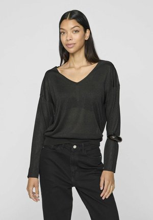 Pull en tricot noir à manches longues avec un décolleté en V, coupe décontractée et texture légèrement transparente, associé à un pantalon noir taille haute.