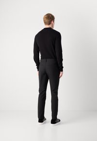 Top de punto negro de manga larga, pantalones ajustados negros, vista trasera. Los pantalones tienen bolsillos en ángulo, se llevan zapatillas negras y blancas.