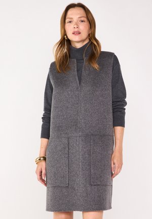 Abito in misto lana grigio con collo alto, scollatura a V anteriore e due ampie tasche a pattina. Le maniche sono in maglia grigia con un design aderente.