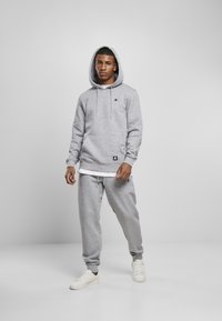 Grijze hoodie met verstelbare koorden, een voorzak en logo. Gecombineerd met bijpassende grijze broek en witte sneakers. Gladde stoftextuur.