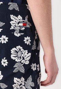 Marineblå shorts med hvite blomstermønstre og prikker. Har en elastisk midje og en baklomme med et rødt og hvitt "Tommy Jeans"-merke.
