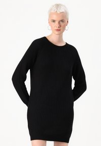 Robe pull noire tricotée à manches longues, avec une texture côtelée et un col rond. Coupe droite, longueur mi-cuisse, sans motifs ni accents.