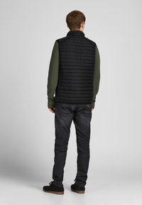 Sort polstret vest med høj krave over en grøn striktrøje. Båret med mørke jeans og sorte sko. Bemærkelsesværdig quiltet tekstur på ryggen.