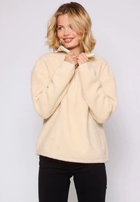 Beżowy polar z półzamkiem przy kołnierzu, długimi rękawami i luźnym krojem. Posiada fakturowaną powierzchnię i boczne kieszenie.