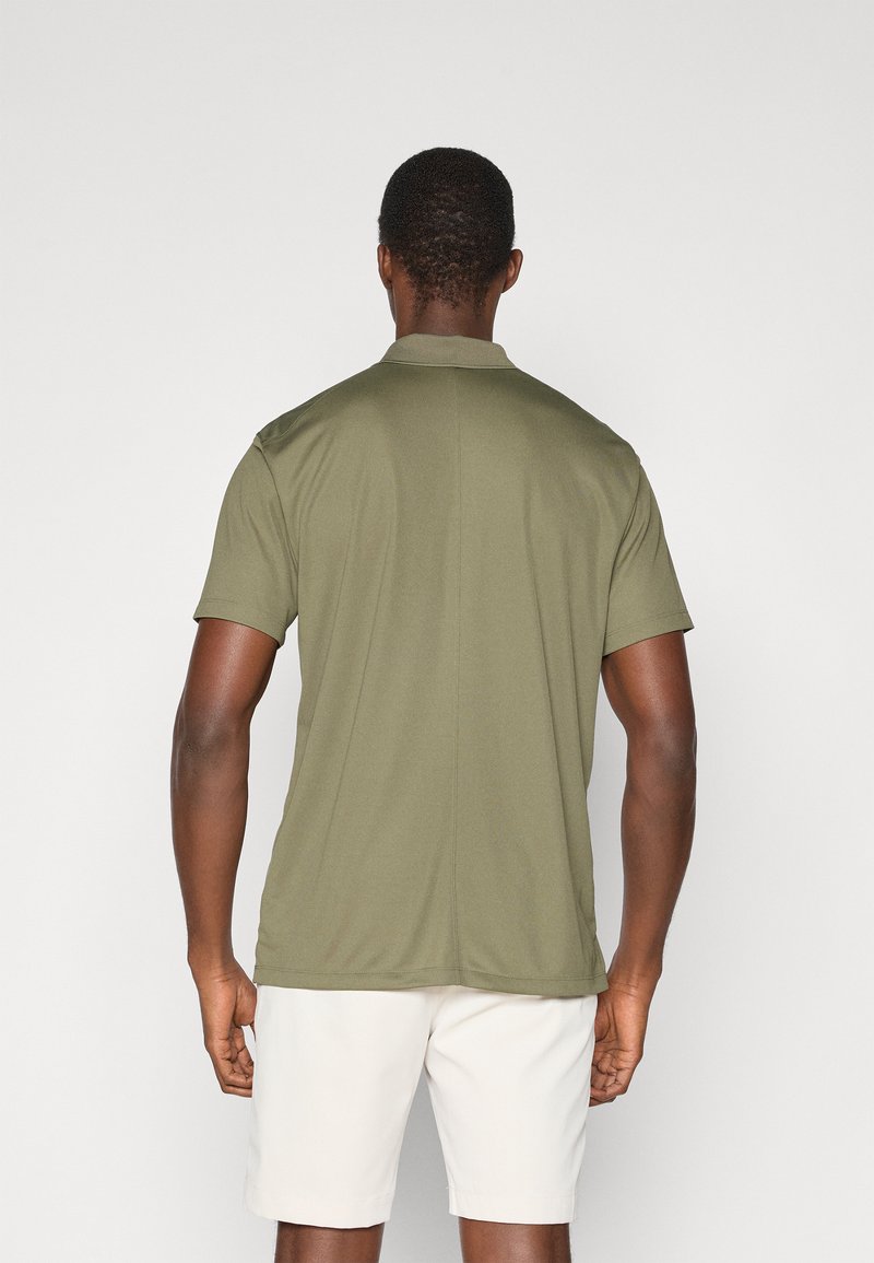 Polo shirt olive green à manches courtes, en tissu léger, col plat, avec une couture au centre du dos. Porté avec un short blanc.