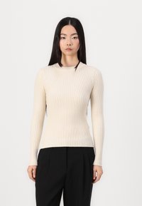 Cream ribbed long-sleeve top featuring a high neckline and slim fit, made of soft, textured fabric. Paired with black trousers.
