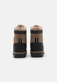 Braune Wildleder- und schwarze Gummiwinterstiefel mit einem gefälschten Fellfutter an der oberen Kante und einer Zuglasche an der Rückseite. Texturiertes schwarzes Gewebe am Knöchel. Robuste Profilsohle.