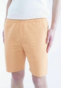 Lys oransje shorts med en teksturert, quiltet mønster, som har elastisk midje og sidelommer for funksjonalitet.